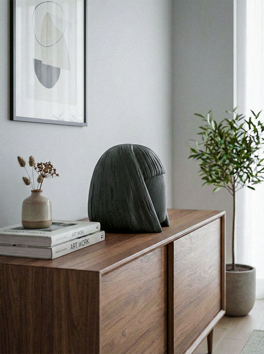 Modern interior with a wooden sideboard, decorative vase, books, and abstract art on a light gray wall.