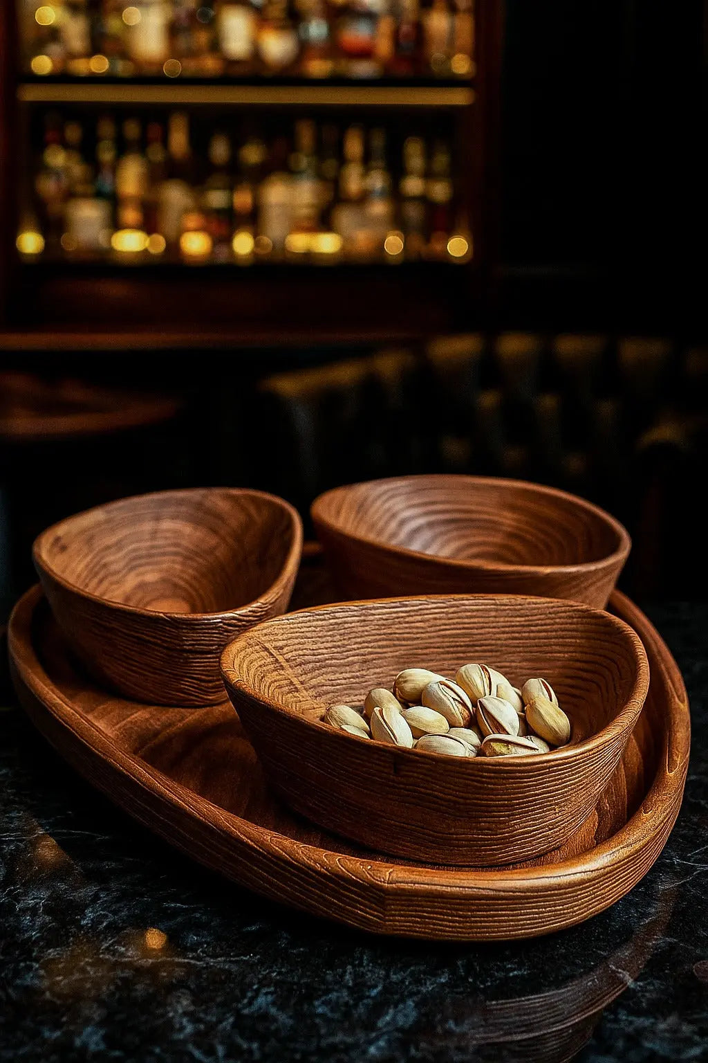 Three woven wooden bowls on a dark surface with a blurred bar background