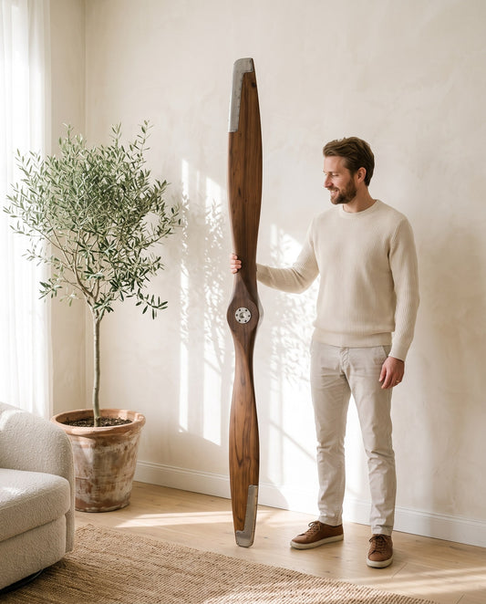 Man standing next to a 180 cm walnut airplane propeller with silver hub to show its real size