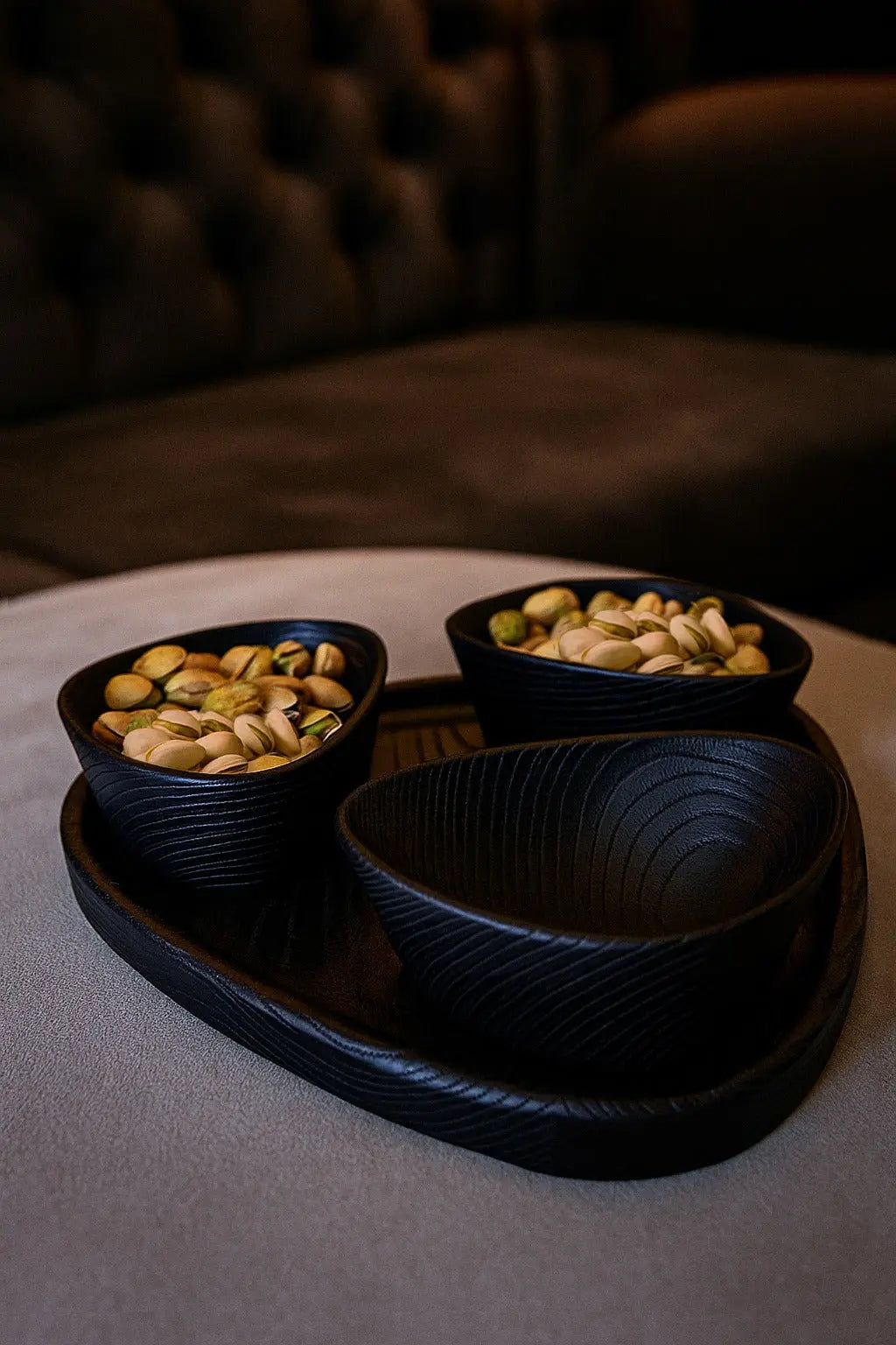 Two black bowls with nuts on a tray on a table.