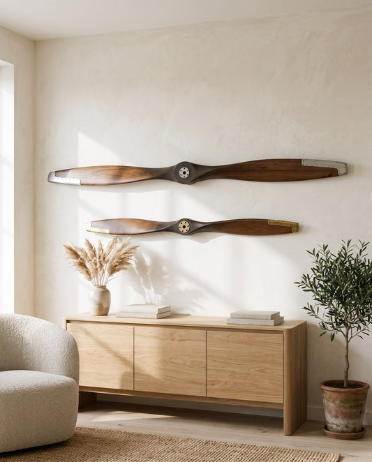 Two wooden airplane propellers, 180 cm with silver hub and 120 cm with brass hub, mounted on a bright living room wall