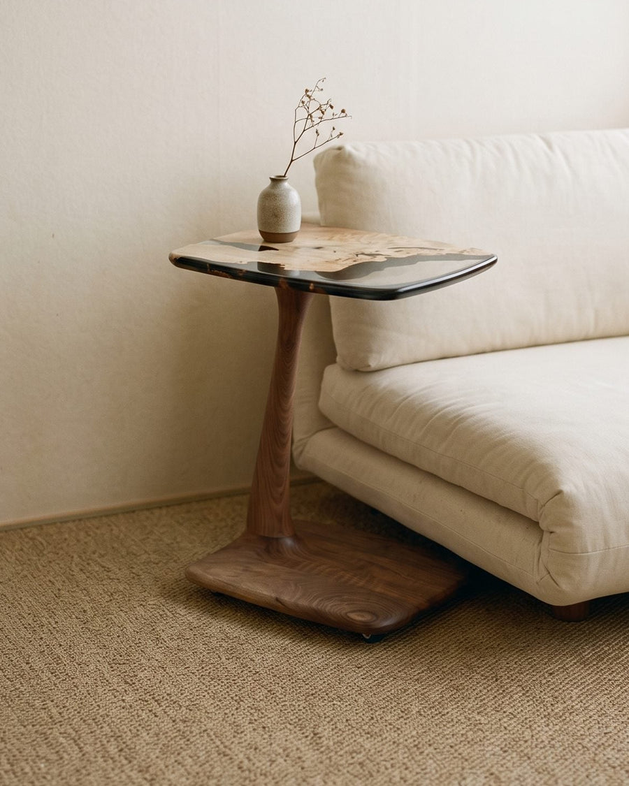 C-shaped walnut and resin end table with its foot tucked under a low cream sofa